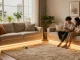 Benzi LED care iluminează un living modern, cu un cuplu ajustând culorile pe smartphone.